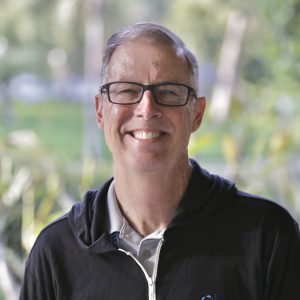 Mark smiling outside in a black zip-up sweatshirt